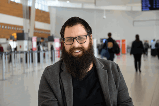 man with beard wearing grey jacket in airport terminal