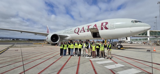 work experience students wearing hi vis vest stand in front of Qatar plane
