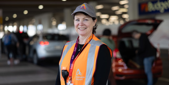 female wearing cap and orange hi vis jacket Infront of cars