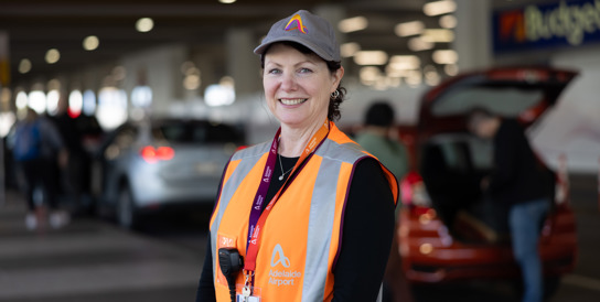 female wearing cap and orange hi vis jacket Infront of cars